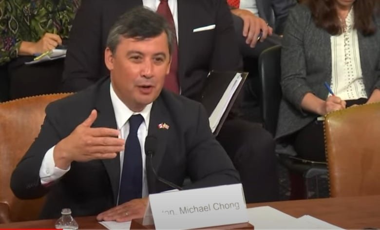 Chong sitting and gesturing while speaking, as people behind him listen or take notes.