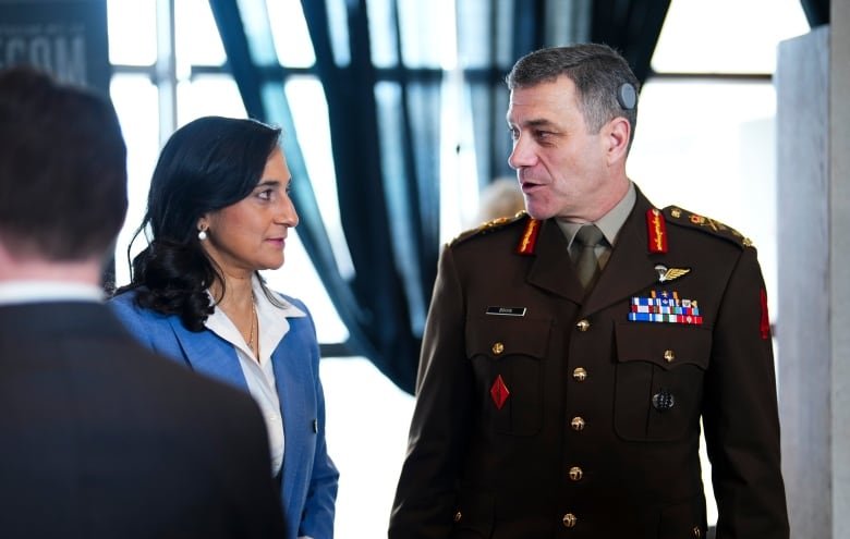 A woman speaks to a man in a military uniform.