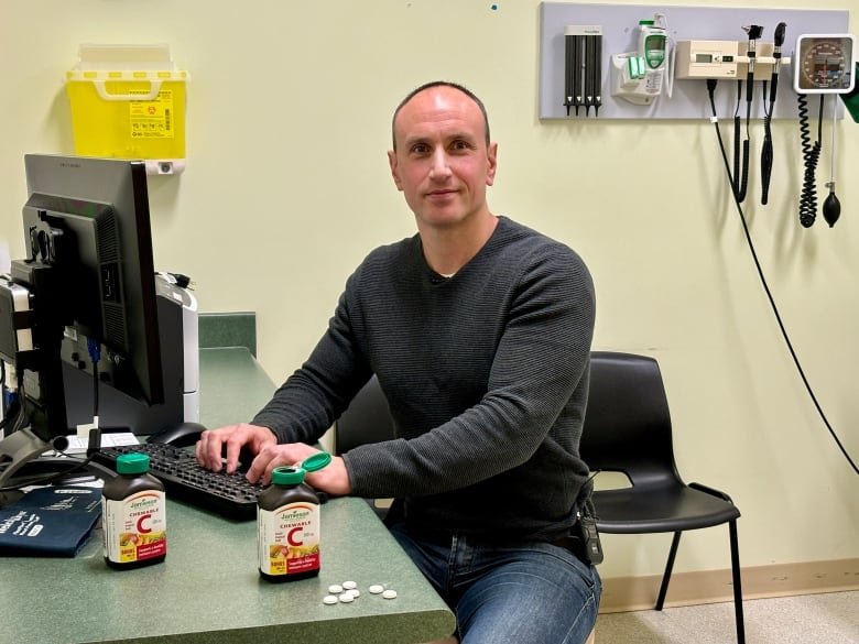 Dr. Jeff Irvine pictured in office with bottles of Vitamin C tablets on his desk