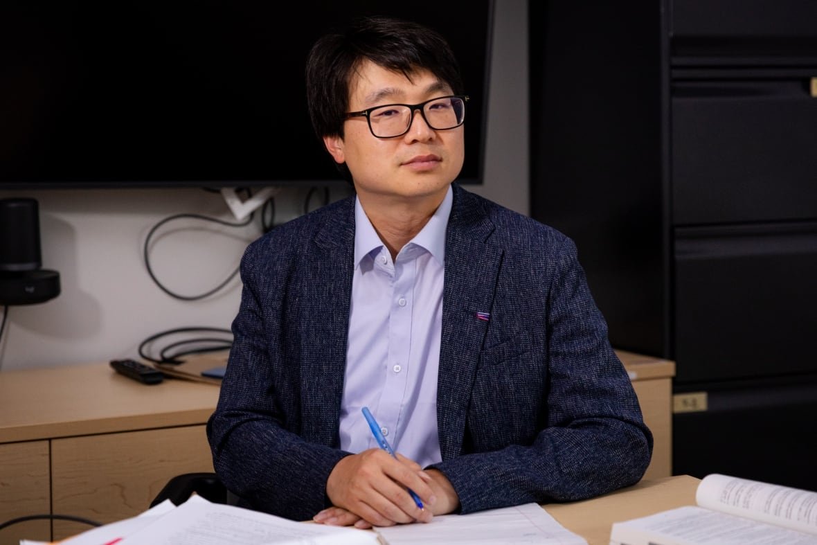 A lawyer sits at a desk with books open and hands folded, one holding a pen.