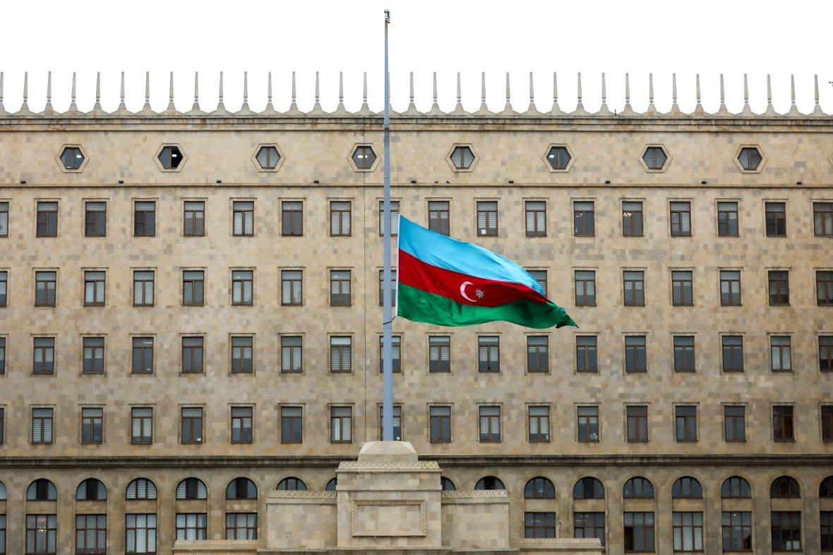 azerbaijan-airliner-crash-5 A blue, red and green striped flag flies at half-mast in front of a grey building.