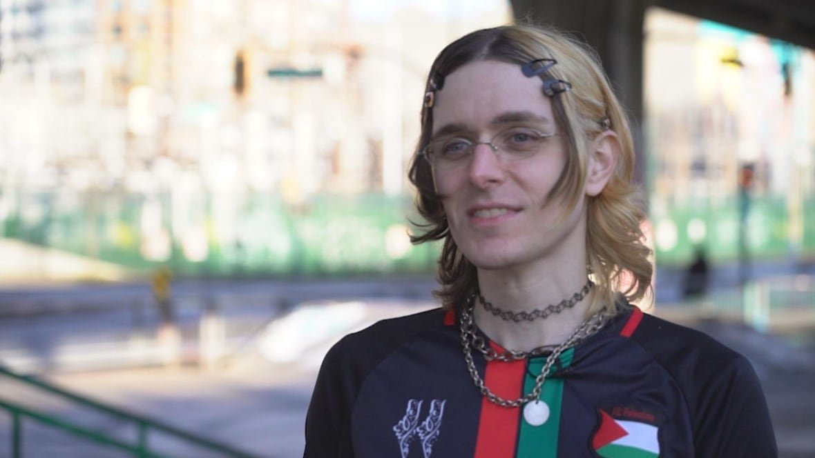 daffodil-street-uni-x-5 A person with blond hair and a black jersey with a Palestinian flag on it smiles.