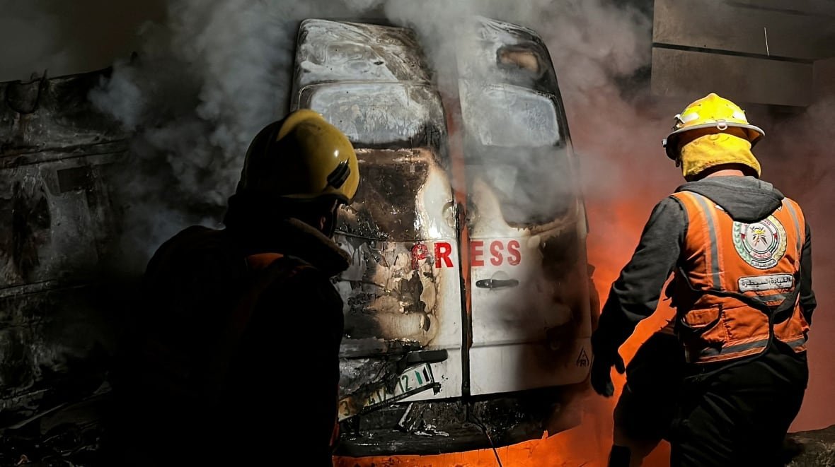 israel-palestinians-gaza-26 Two emergency workers approach a smoking vehicle with the word Press printed on its back doors.