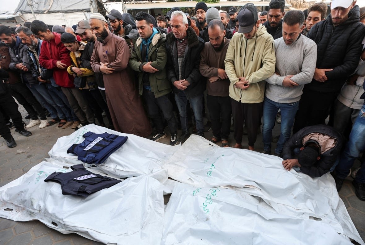 israel-palestinians-gaza-27 Flak jackets are laid on top of two bodybags. A line of people stand over them paying their respects.