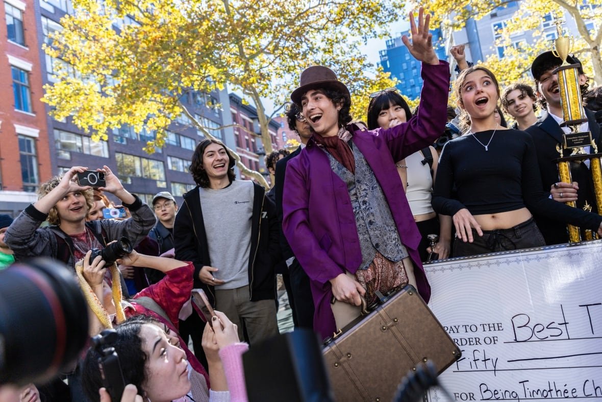new-york-chalamet-look-alike-contest-1 Timothee Chalamet lookalike contest in New York. man celebrates in front of outdoor crowd dressed as the actor in Wonka.