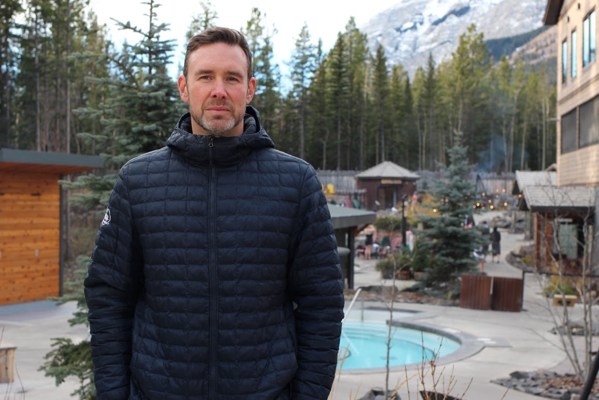 ryan-pomeroy A man in a black puffer jacket poses for a photo at an outdoor Nordic spa in Kananaskis, Alta. with mountains in the background.