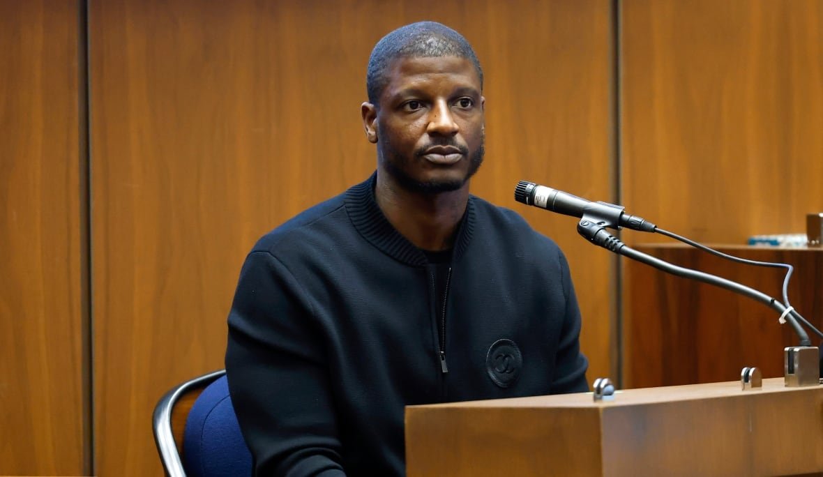 A man sits at a wooden podium with a microphone pointed at him.
