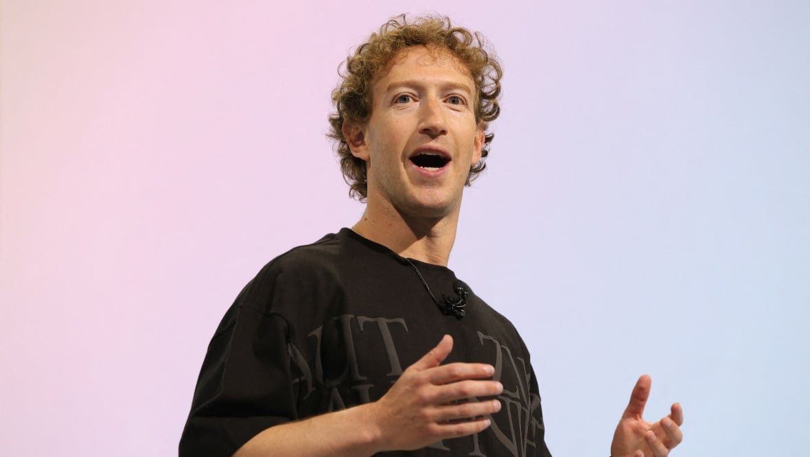 meta-platforms-virtual-reality A man stands in front of a pastel background, clearly mid-speech, with raised arms.