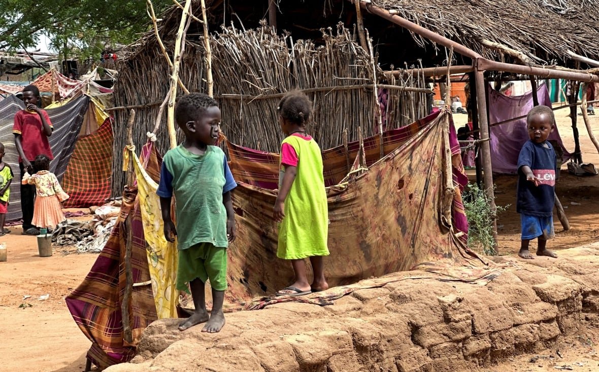 sudan-famine-security-1 Small children are seen walking around makeshift huts on the dirt-covered ground.