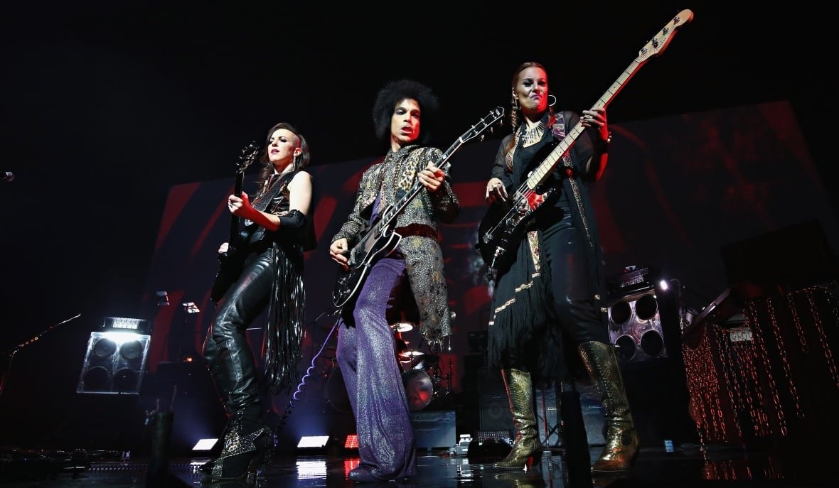 474585200 A man and two women stand side by side playing guitars on a concert stage.