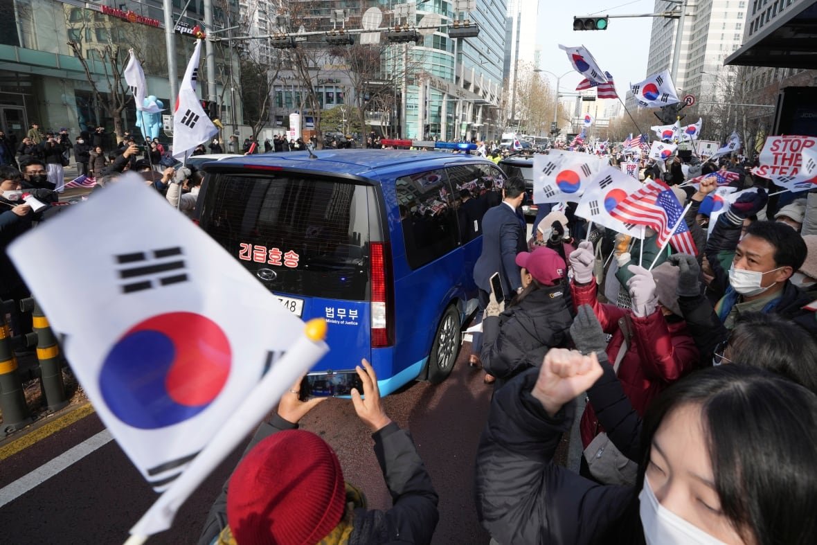 aptopix-south-korea-martial-law A large crowd of people waving flags surround a car.