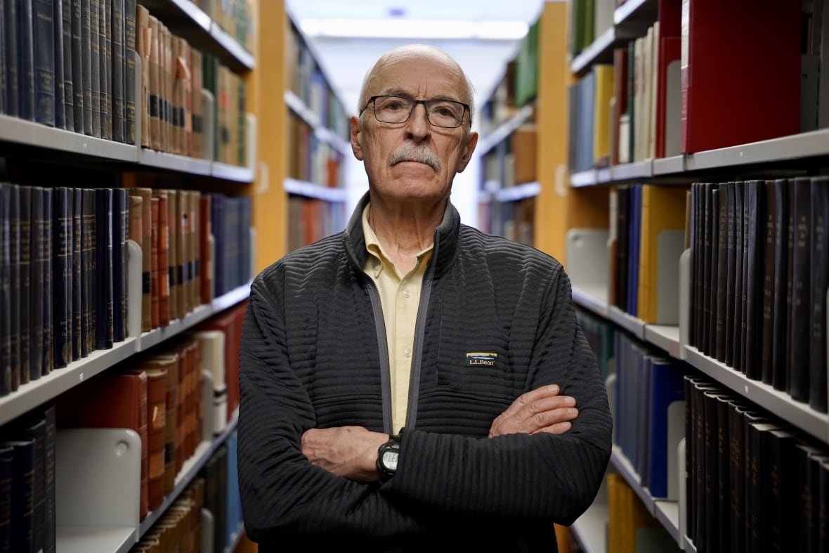 archie-kaiser man poses between two rows of books with his arms folded.