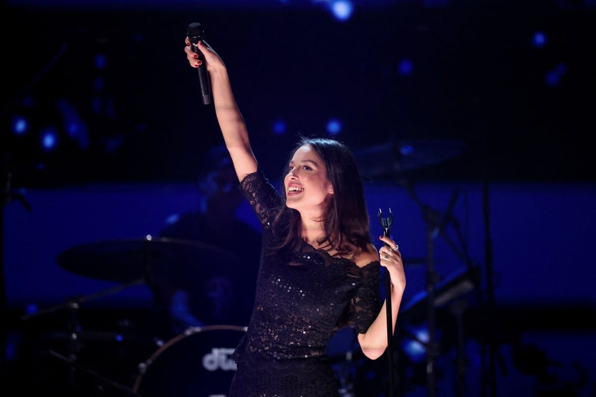 california-wildfires-concerts-3 A young woman smiles on a stage and holds up a microphone.