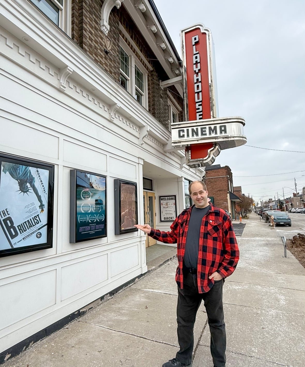 daryl-granger-at-playhouse A person stands on a sidewalk by a theatre with a sign reading "Playhouse Cinema" and points toward the building.