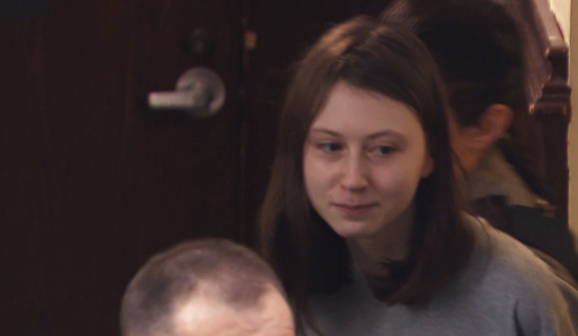 elliott-chorny Woman with medium-length straight brown hair in a grey t-shirt