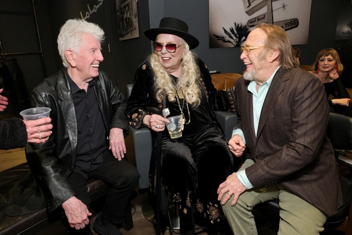 fireaid A woman with long blond hair sits on a chair. Two men sit on either side of her