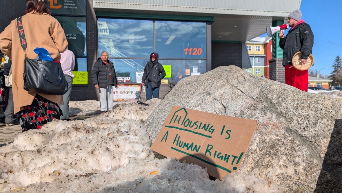 homelessness-advocacy-march-saskatoon-march-1-2025-1 people stand outside with a sign in the foreground that says "Housing is a human right."