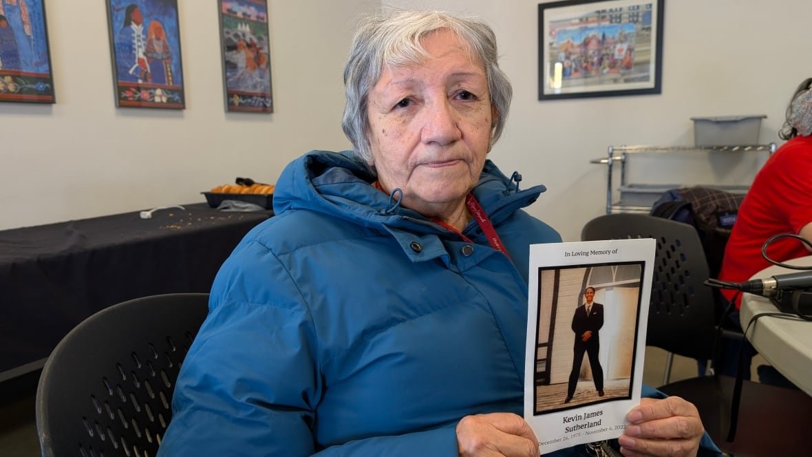 irene-head-saskatoon-1 A woman in a jacket holds up an obituary card of her son