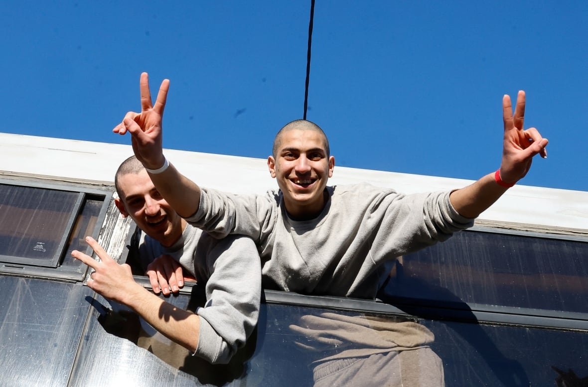 israel-palestinians-gaza-ceasefire-1 Two men stick their heads out of a bus doing a peace sign.