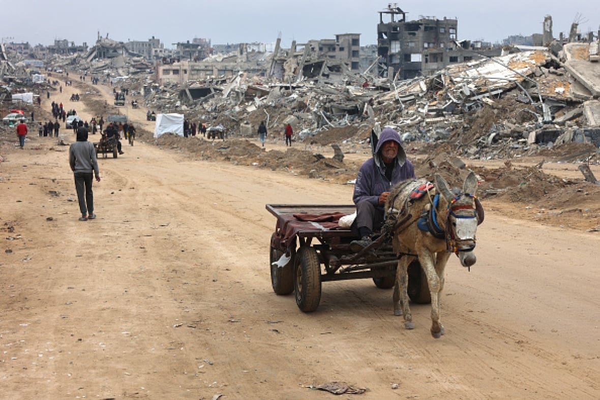jabalia-gaza-3 A man rides in a donkey-pulled cart past the rubble of destroyed buildings.