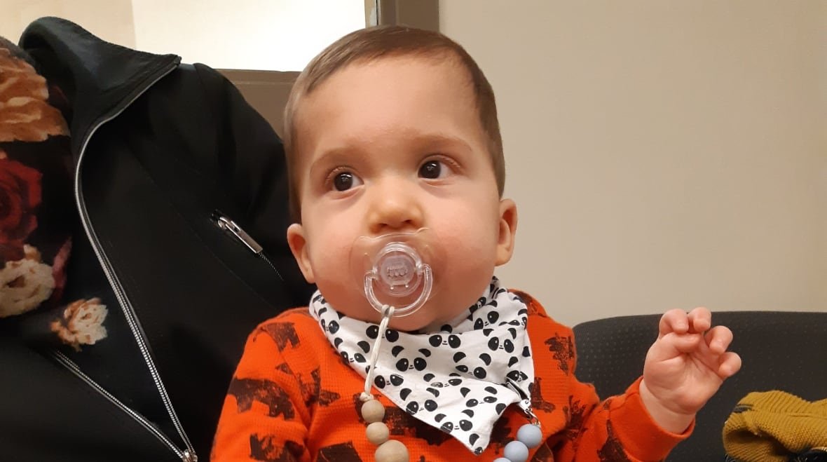 max-seccia-smith-1 An infant with a pacifier in his mouth balances on an adult's lap.