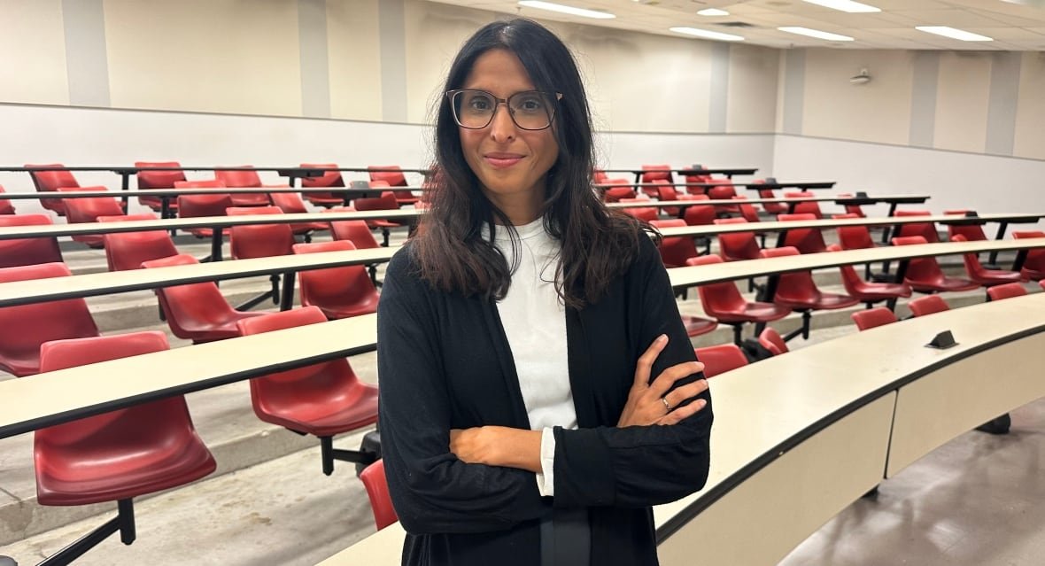rupa-banerjee Photo of Rupa Banerjee standing in front of empty desks in a classroom.