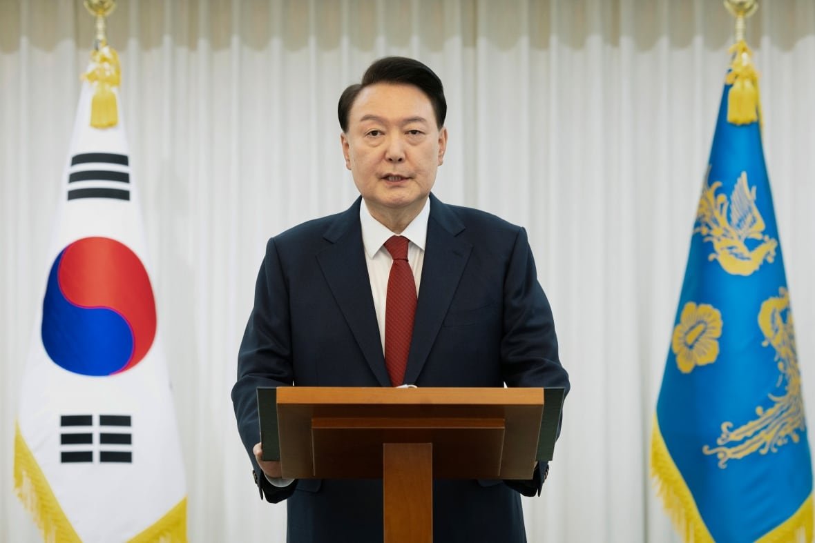south-korea-martial-law A person speaks at a lectern as flags are seen behind them.