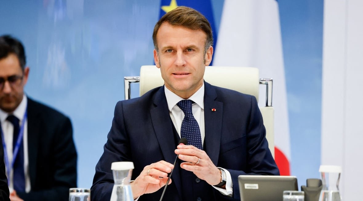 storm-chido A man in a suit is in the centre of the image, with another man visible at the left side of the image. The man in the centre appears to be in the middle of speaking or about to speak and has both hands slightly raised near the microphone on the desk he is sitting at.