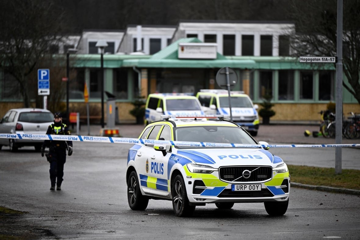 sweden-crime-5 Police officers and vehicles are seen in a parking lot cordoned off by police tape.