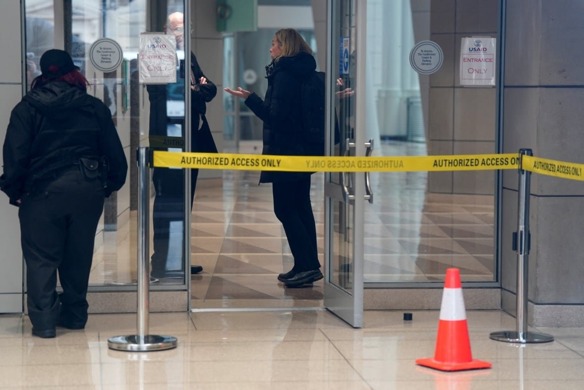 usa-trump-aid Yellow tape is shown outside a building entrance, with a woman visible inside speaking as a man looks on.