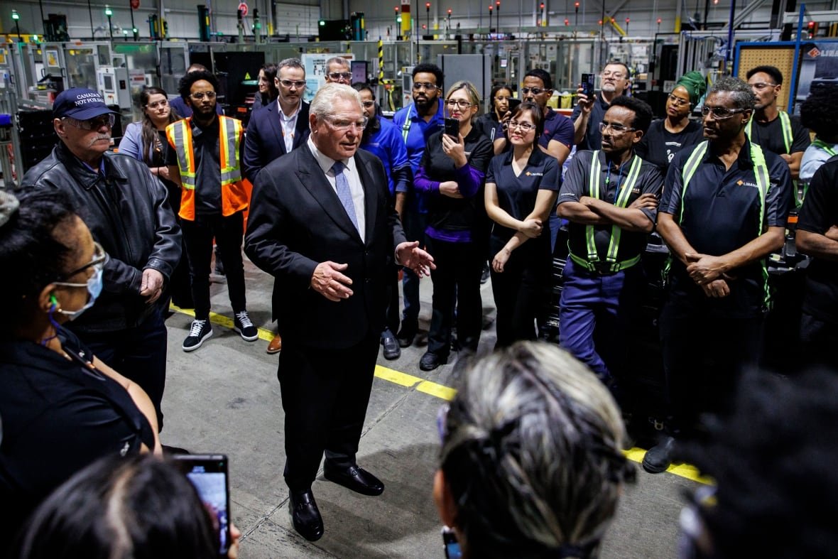 doug-ford-ontario-election-linamar-auto-parts A man in a suit stands in a factory setting with workers around him looking at him as he speaks
