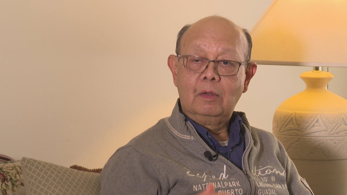 koko-kyi A bald man in glasses, senior age, sits in his living room and speaks to someone off camera