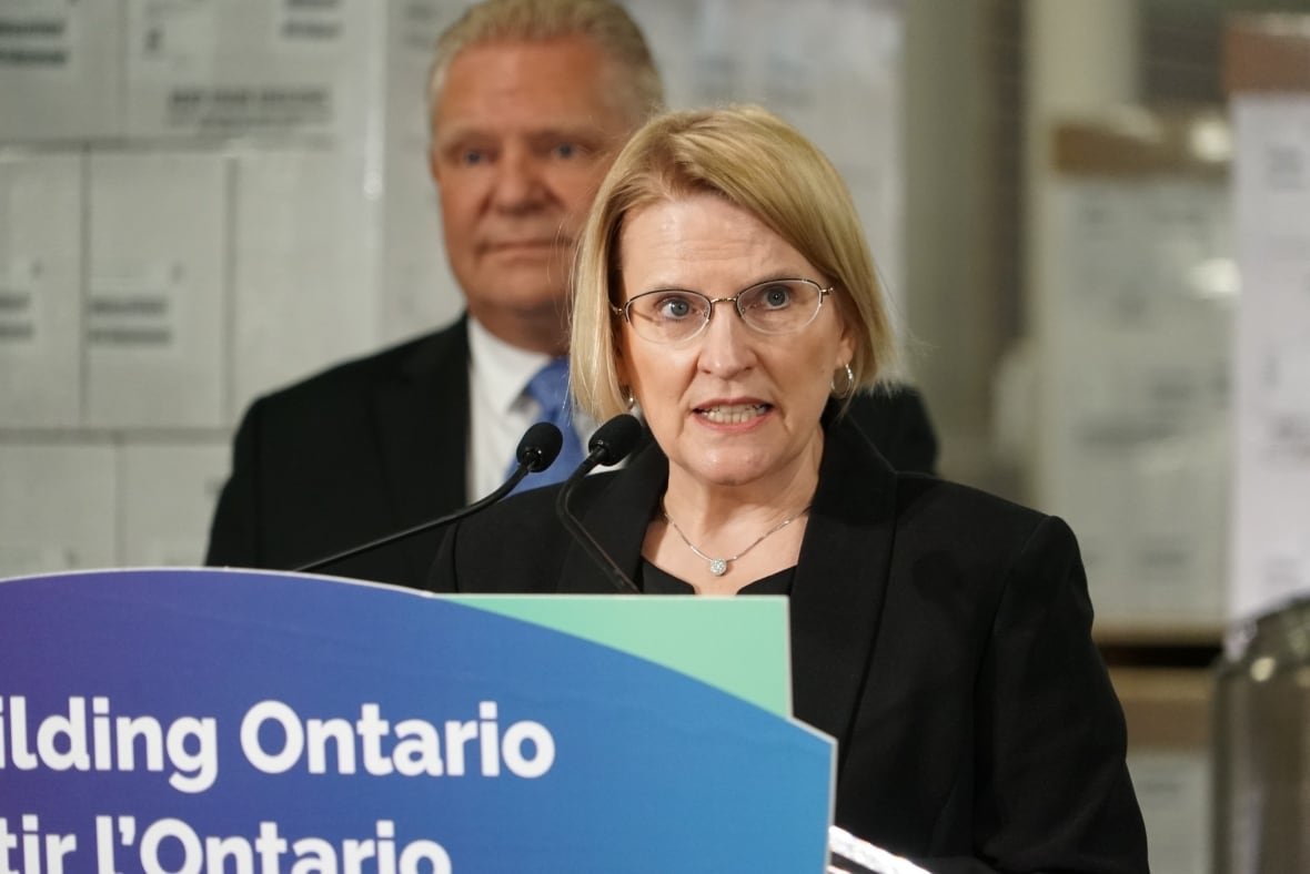 ontario-health-minister-sylvia-jones A woman stands in front of a microphone and podium at a news conference.