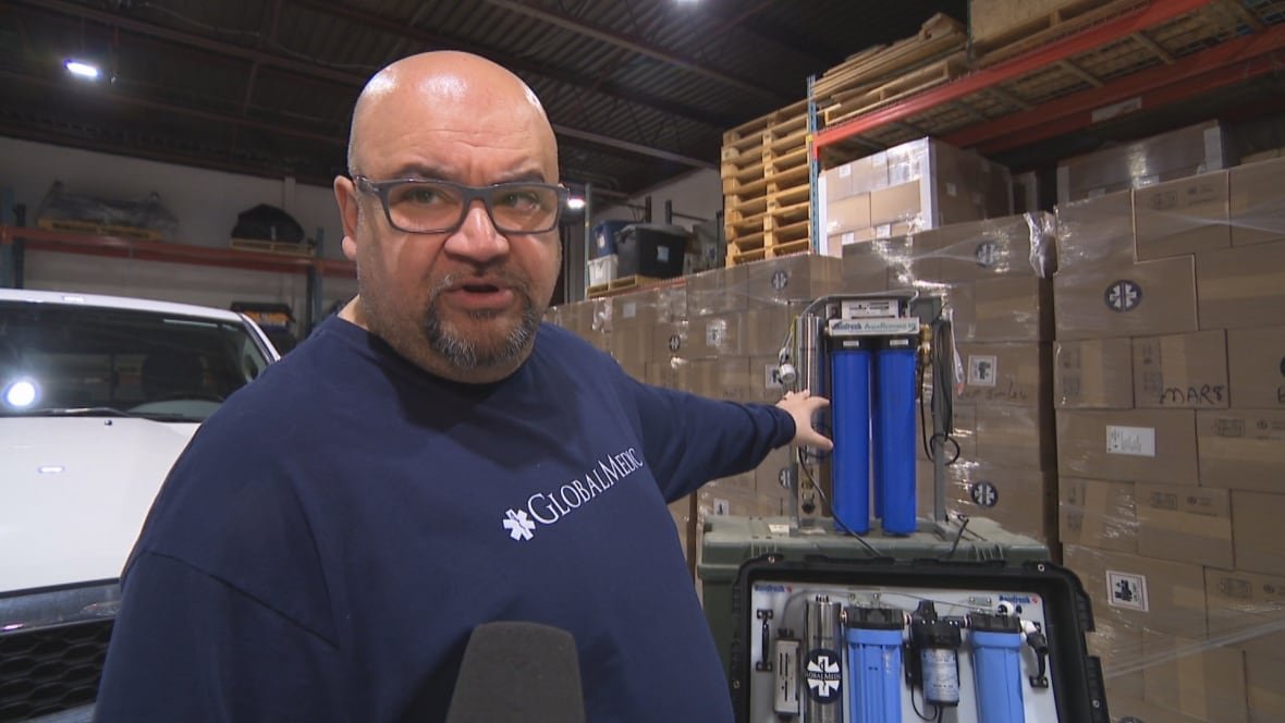 rahul-singh A man in a Global Medic shirt in a warehouse points at a water purifier