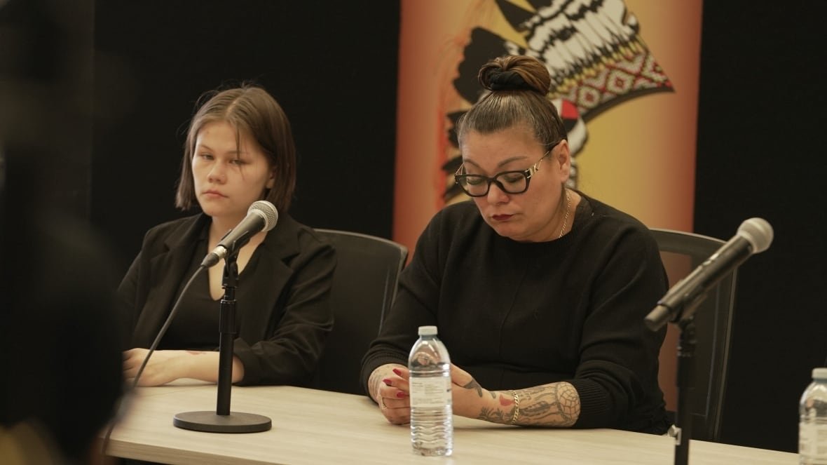 amc-press-conference-feb-27 Two women with sombre expressions sit behind microphones on a table.