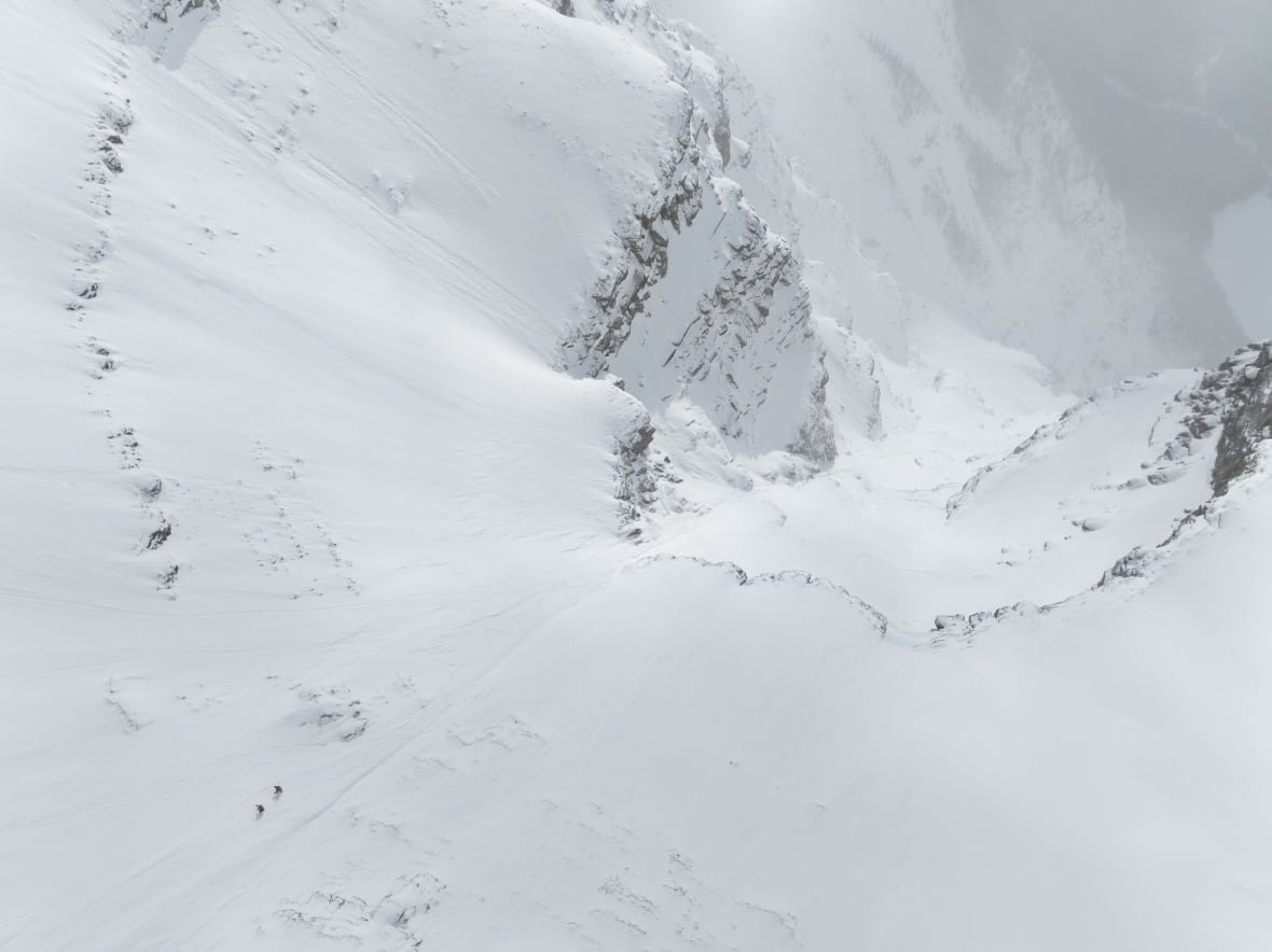 christina-lusti-lustenberger-guillaume-pierrel-ascend-mount-robson-1 A wide aerial shot of a snowy slope with two tiny people traversing it.