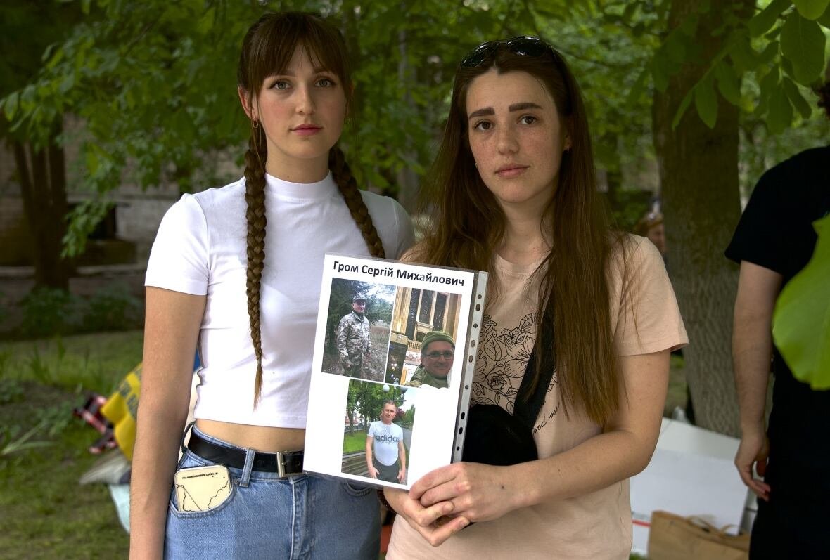 iryna-mylto-holding-photo-and-her-sister-olena-kachaeva-1 Two people pose for a photo as one of them holds up a collage of portraits.
