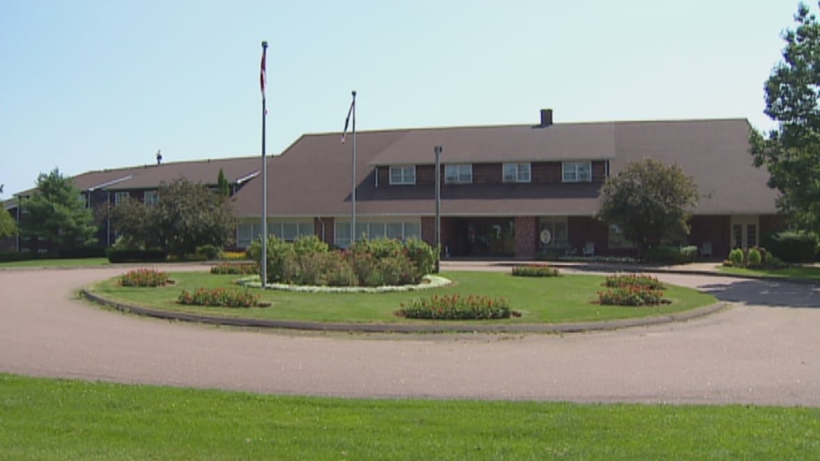 mill-river-resort A circular patch of grass with plants and two flag poles in front of a brown building with a brown roof.