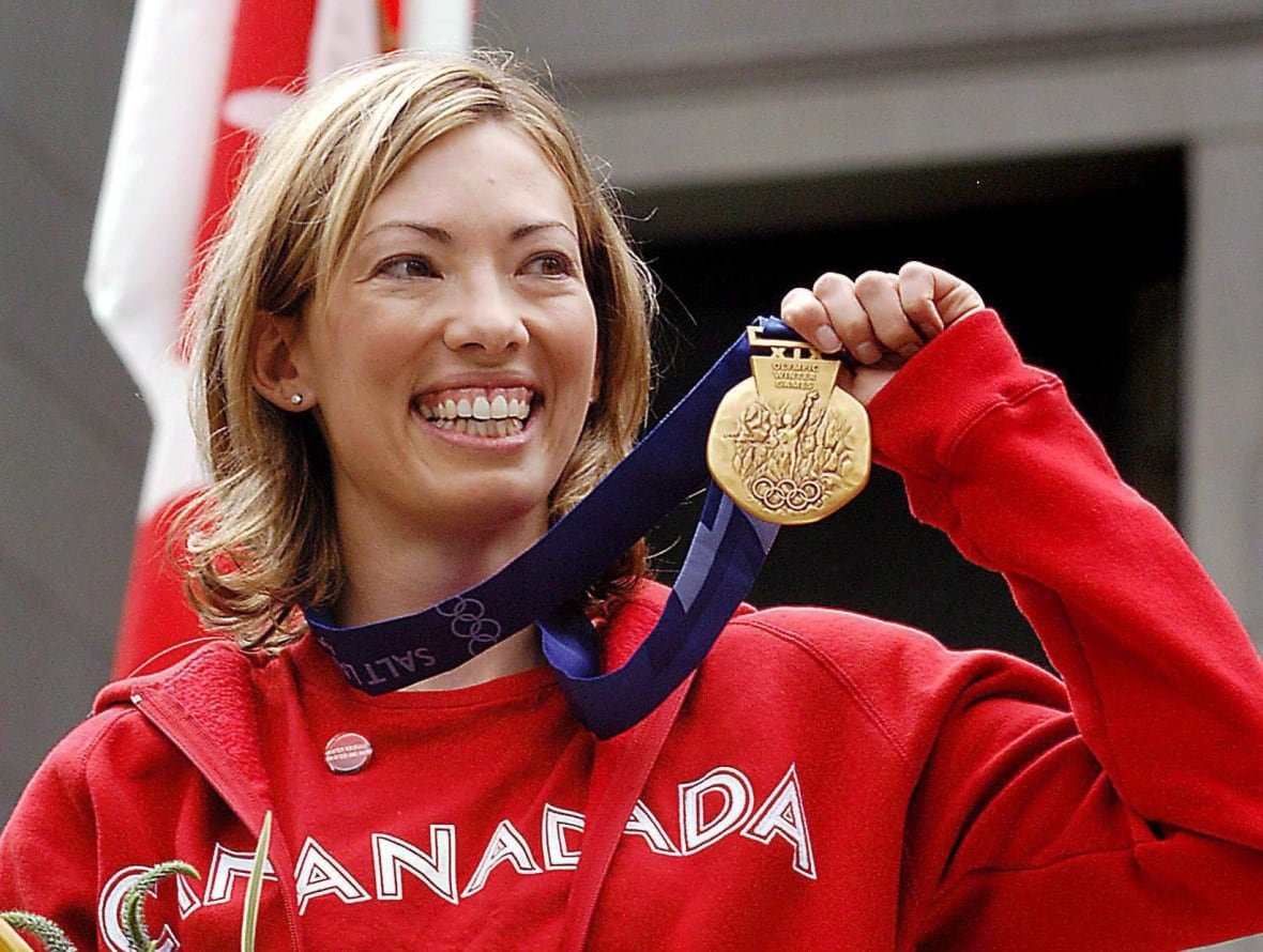 ski-crosscountry-scott A blond haired person wearing a red top with Canada on it, smiling, and holding up a medal.