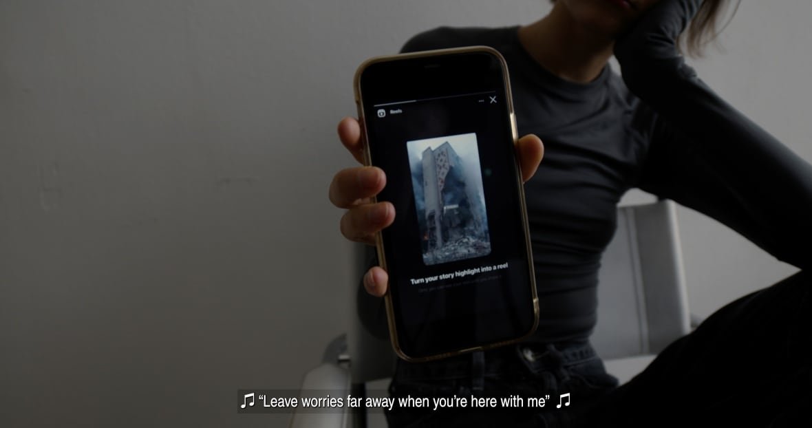 the-longer-you-bleed-1 A woman holds up a phone to the camera. On it, a blown-up building is shown. Underneath photo of the building are the words 'Turn your story highlight into a reel.'
