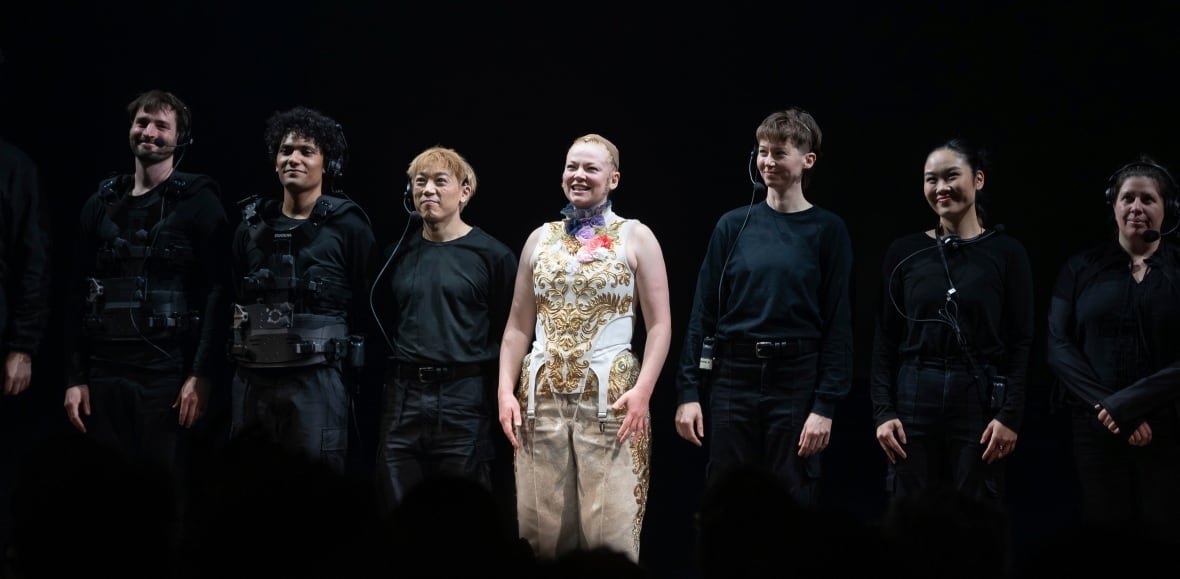 the-picture-of-dorian-gray-broadway-opening-night-1 A line of people are shown, almost all of them wearing black, except for a woman in the centre, who is wearing a bright white and patterned outfit.