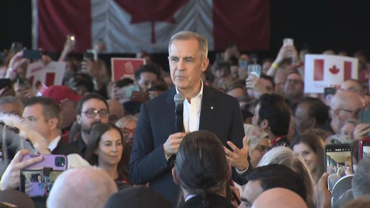 carney-saskatoon A grey-haired man in a suit speaks on stage.