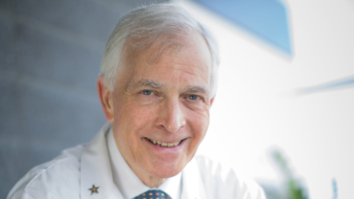 dr-anthony-lang-neurologist-toronto-1 A portrait of a smiling man with grey hair, wearing a white doctor's coat, a white collared shirt and a blue tie.