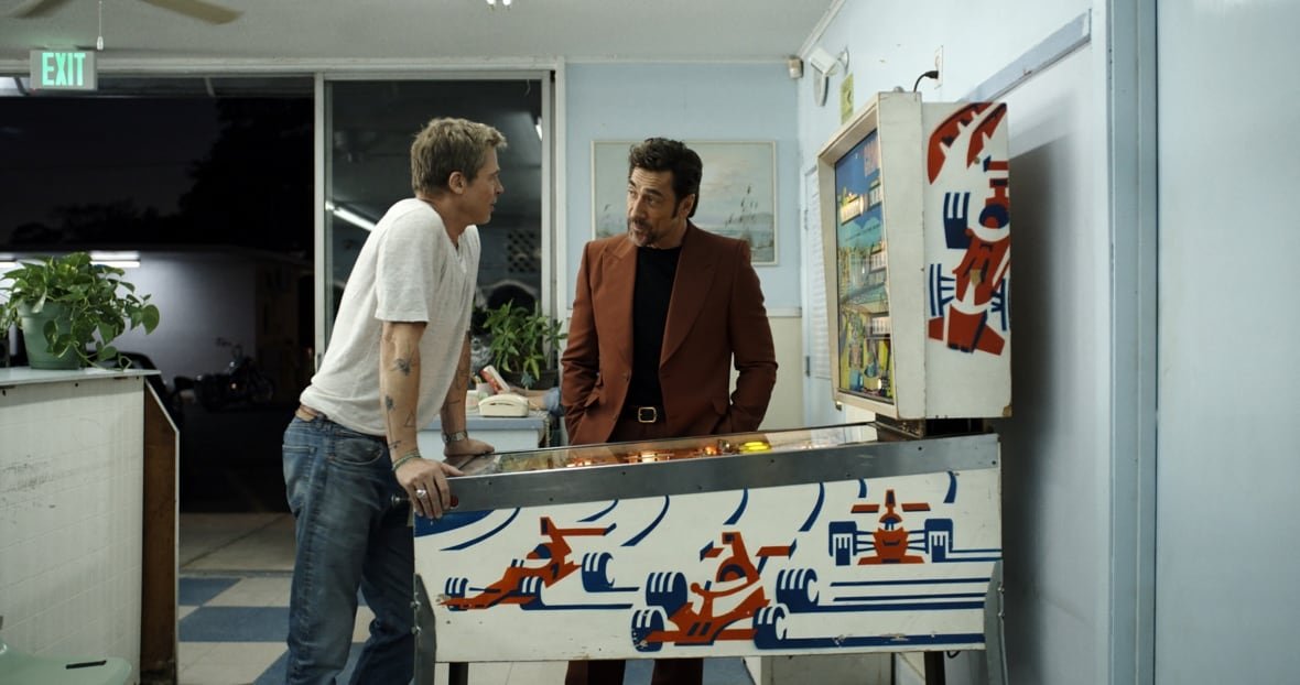 f1-the-movie-4 Two men stand in front of a pinball machine.