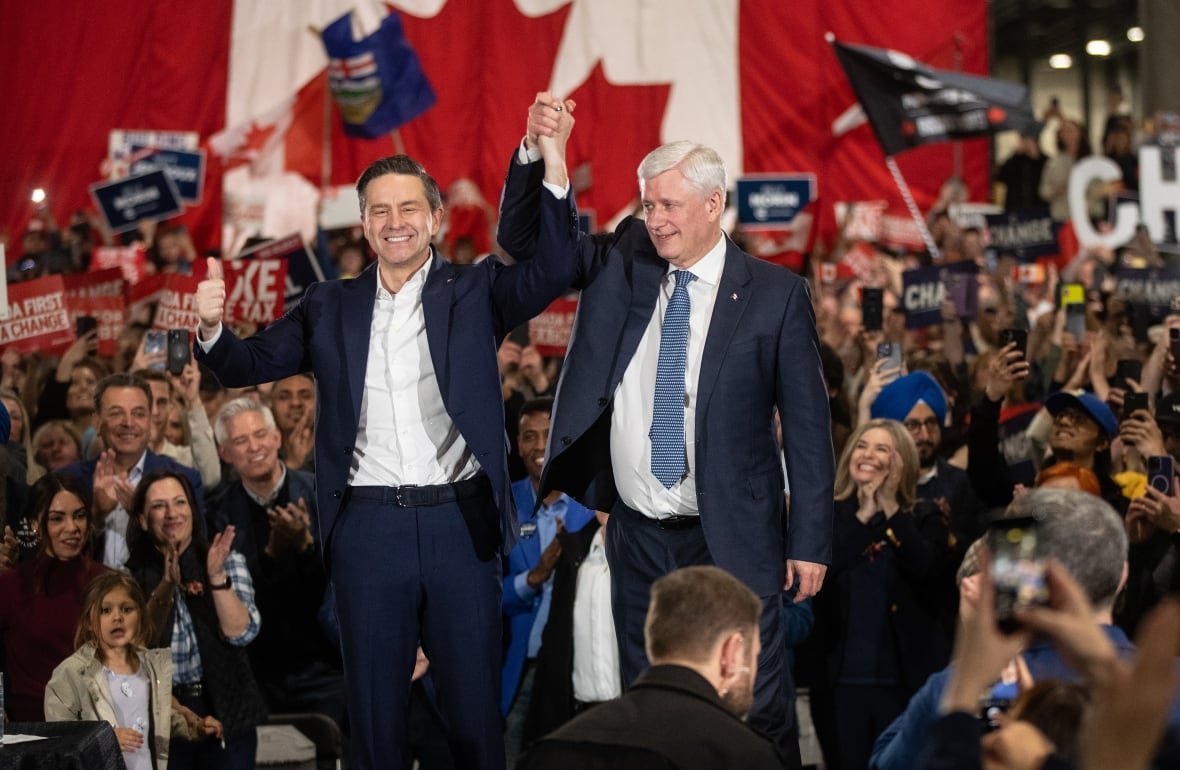 fedelxn-conservative-20250407 Former prime minister Stephen Harper and Conservative Party Leader Pierre Poilievre are pictured standing side-by-side on a stage, raising clasped hands. They are surrounded by a crowd of people.
