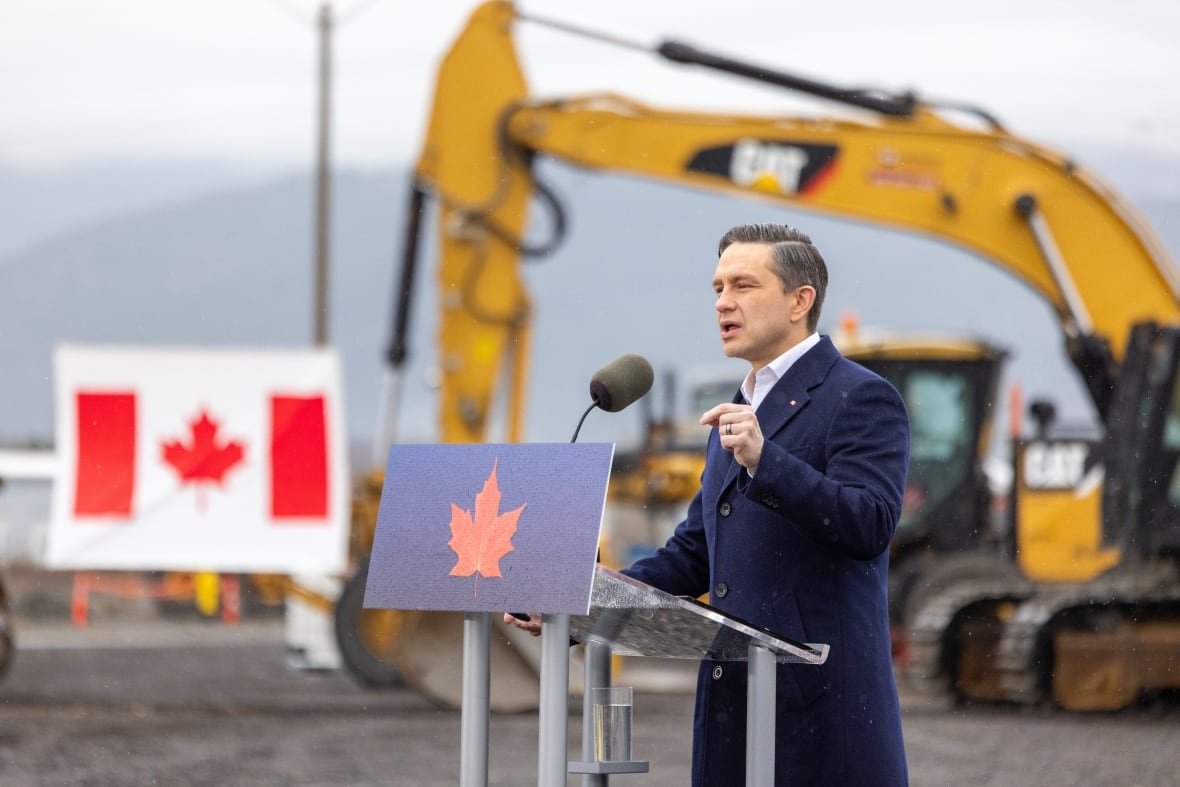 fedelxn-conservatives-20250407-pierre-poilievre-2 A man wearing a blue coat speaks at a podium, with a Canadian flag and front loaders behind him.