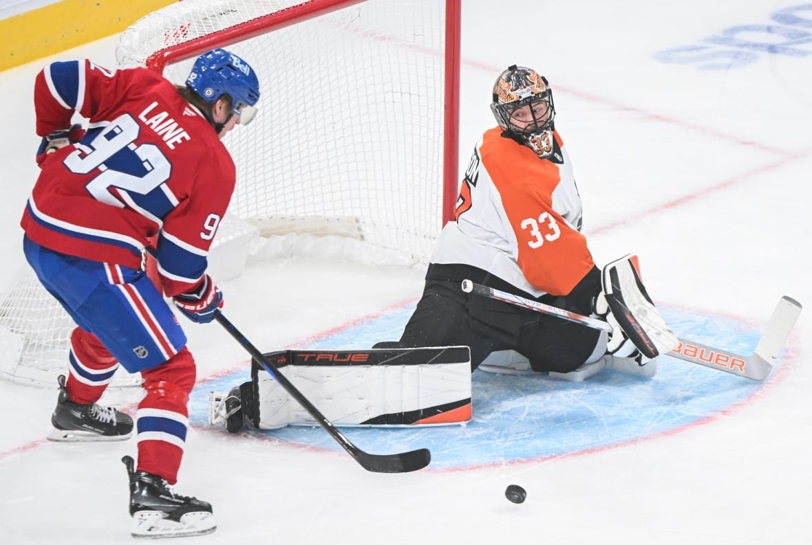 hkn-flyers-canadiens-20250405-3 A hockey player stands in front of a goaltender as a puck is loose in front of the net