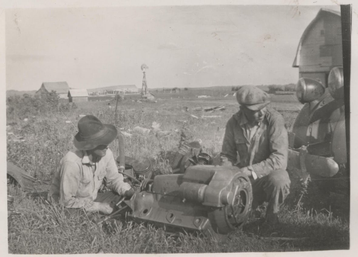 jason-jackson-5 Two men lay on the grass repairing a piece of equipment in this black and white photo.