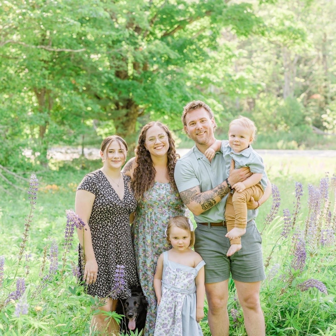 macmillan-family A smiling group of five people and a dog pose for a family photo in a grassy field.
