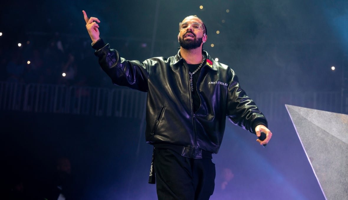 music-drake-tour-20241125-1 A man stands onstage, with one hand lifted up, finger pointed, in the middle of talking or singing.